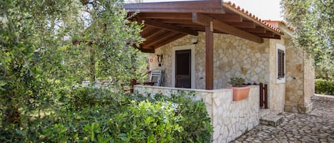 Un edificio de piedra con una pérgola de madera, rodeado de vegetación.