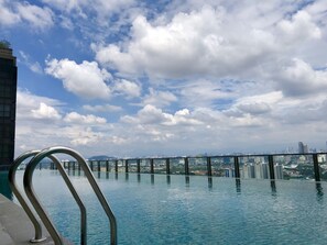 Une piscine à débordement offrant une vue sur les gratte-ciel de la ville, avec des garde-corps en métal et un ciel partiellement nuageux.