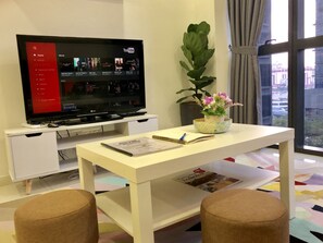 A hotel room with a flat-screen TV displaying YouTube, a white desk with a notebook, a pen, and a potted plant.