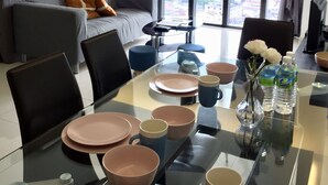 Un salón moderno con una mesa de comedor de cristal, un sofá gris y vistas a la ciudad a través de grandes ventanales.