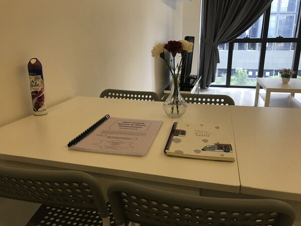 Une table avec un carnet, un stylo, une canette de boisson et un vase de fleurs.