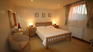 A bedroom with a wooden bed, two bedside tables with lamps, a chair, a mirror, and a window with curtains.