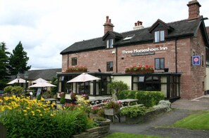 A brick building with a sign reading "Three Horseshoes Inn" and outdoor seating with umbrellas. - Three Horseshoes Country Inn and Spa (Leek)