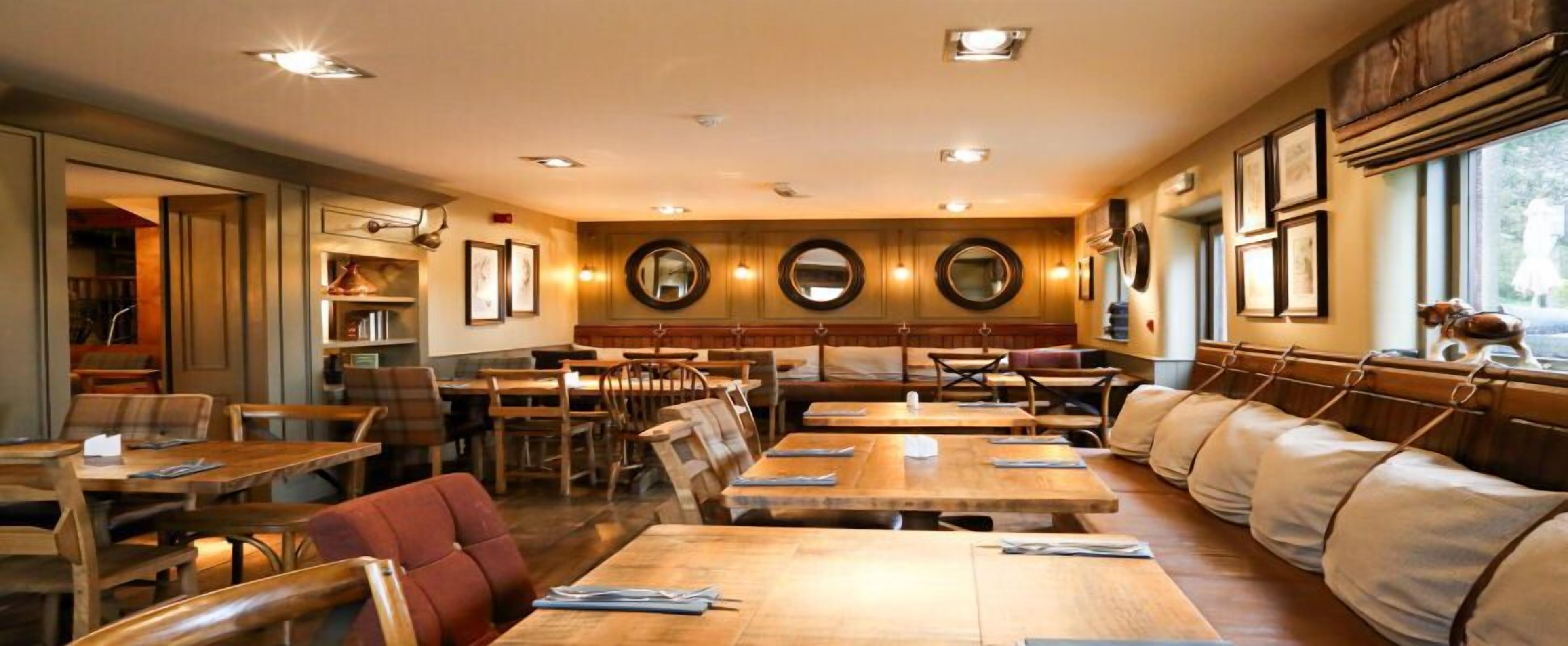 A restaurant with wooden tables and booths, framed mirrors on the walls, and a view of the outdoors through large windows.