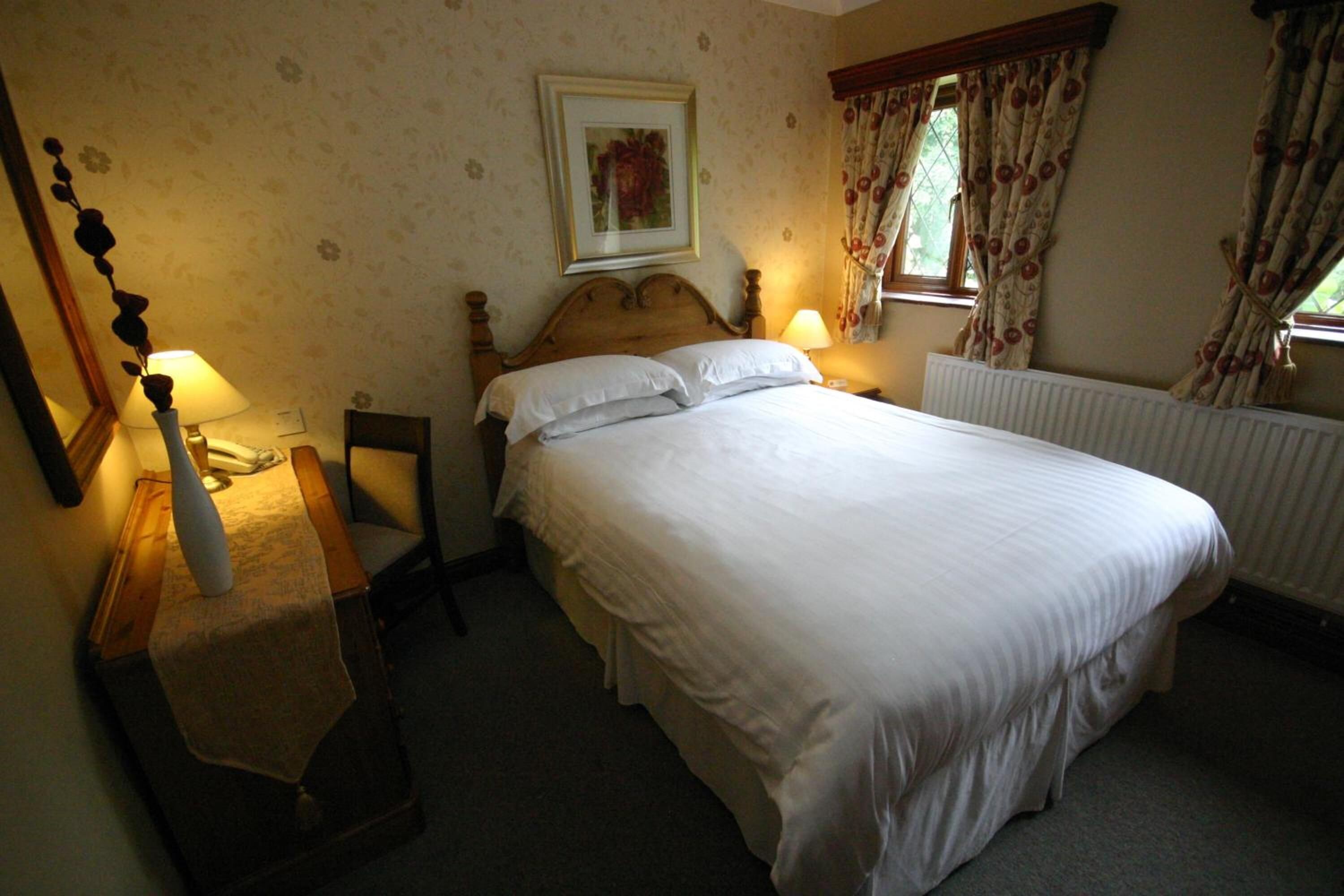 A bedroom with a large bed, a nightstand, a chair, a framed picture on the wall, and a window with curtains.