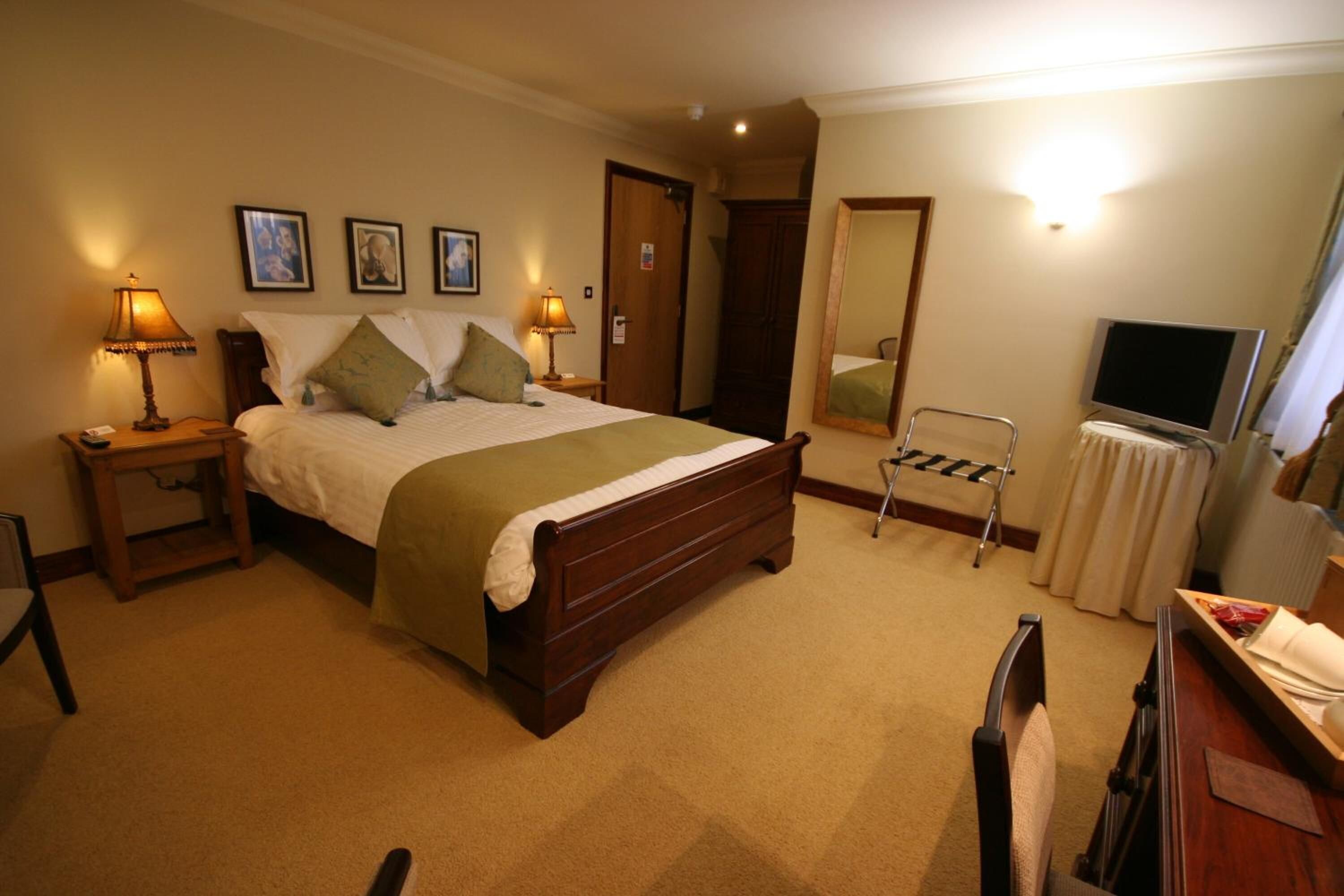 Habitación de hotel con una cama grande, dos mesitas de noche con lámparas, una silla, un escritorio con espejo y un televisor.