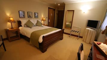 Habitación de hotel con una cama grande, dos mesitas de noche con lámparas, una silla, un escritorio con espejo y un televisor.