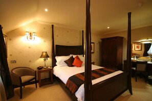 A four-poster bed with a headboard, a bedside table with a lamp, a chair, and a desk with a mirror. - Three Horseshoes Country Inn and Spa (Leek)