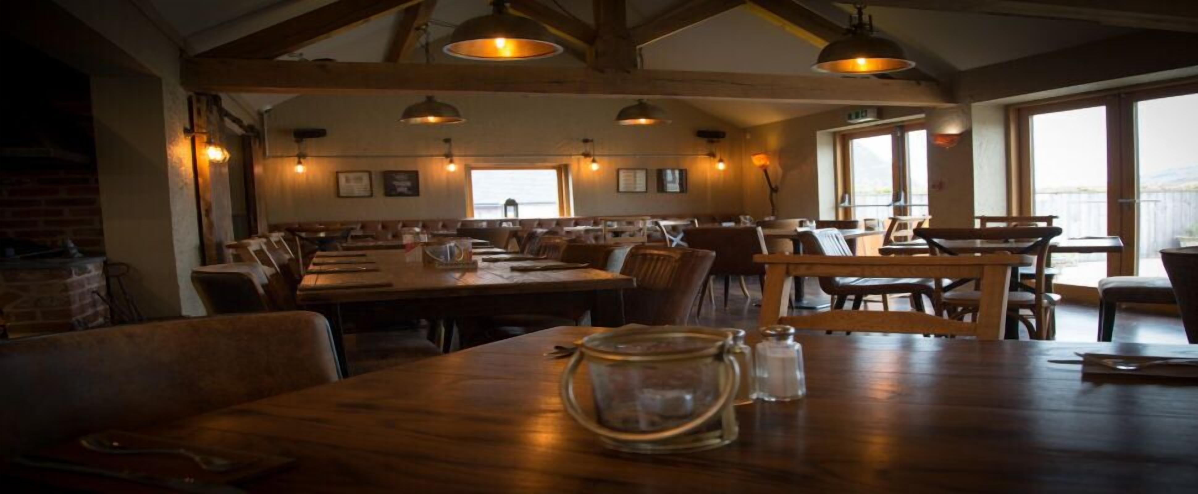 Un restaurant avec des tables et des bancs en bois, des luminaires suspendus et de grandes fenêtres.