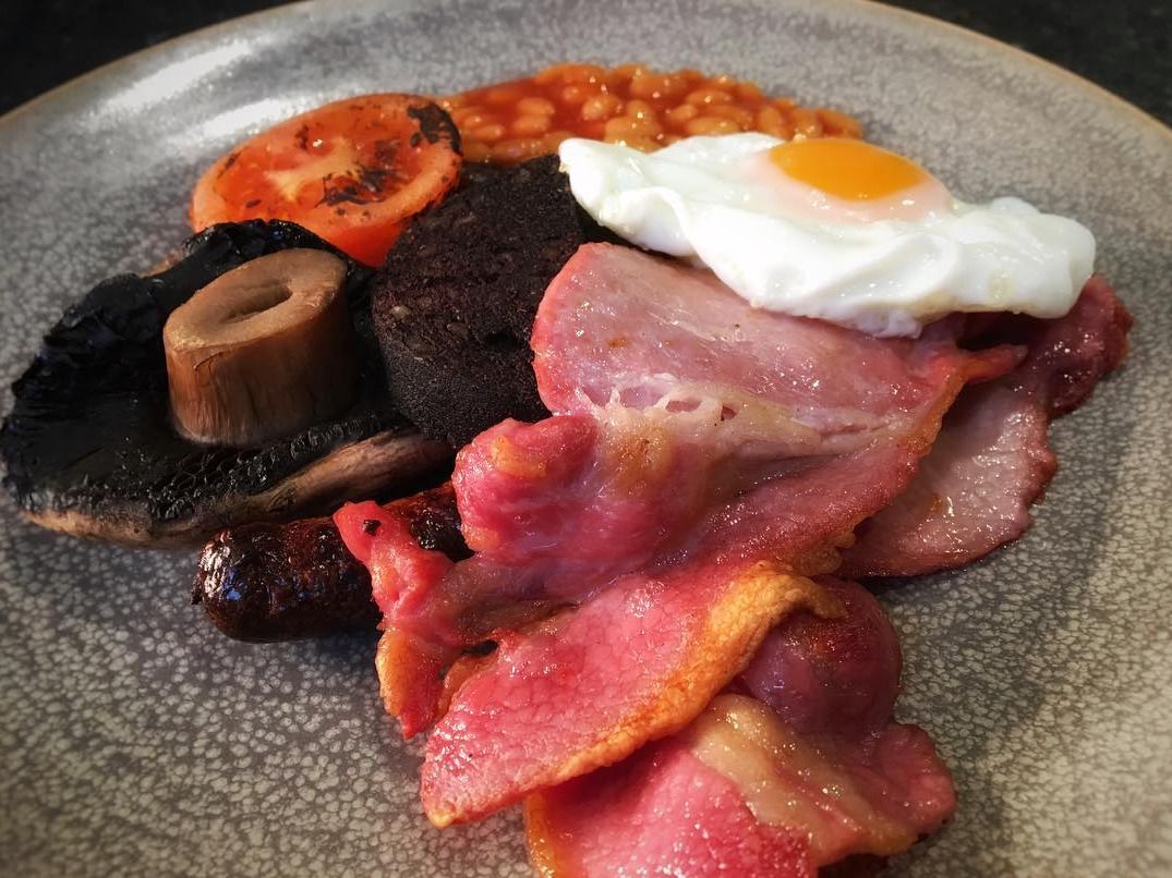 En tallerken med spejlæg, bacon, svampe, blodpølse, bønner i tomatsovs og en grillet tomat.