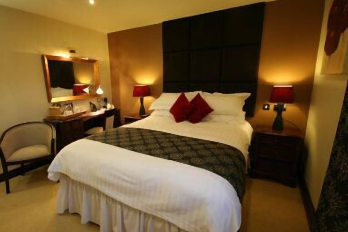 Quarto de hotel com uma cama grande, uma escrivaninha, uma cadeira e um espelho.