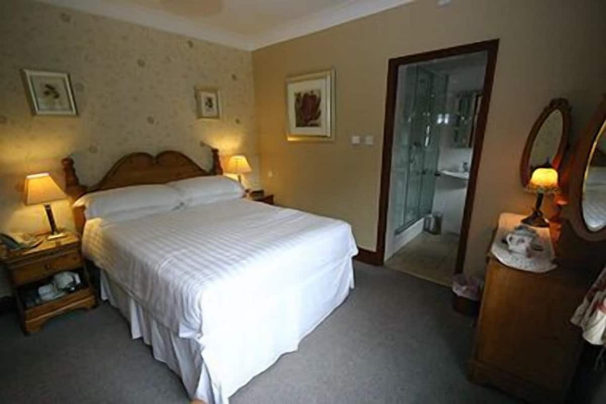 Quarto de hotel bem arrumado, com cama, luminárias laterais, cômoda, espelho e porta para um banheiro.