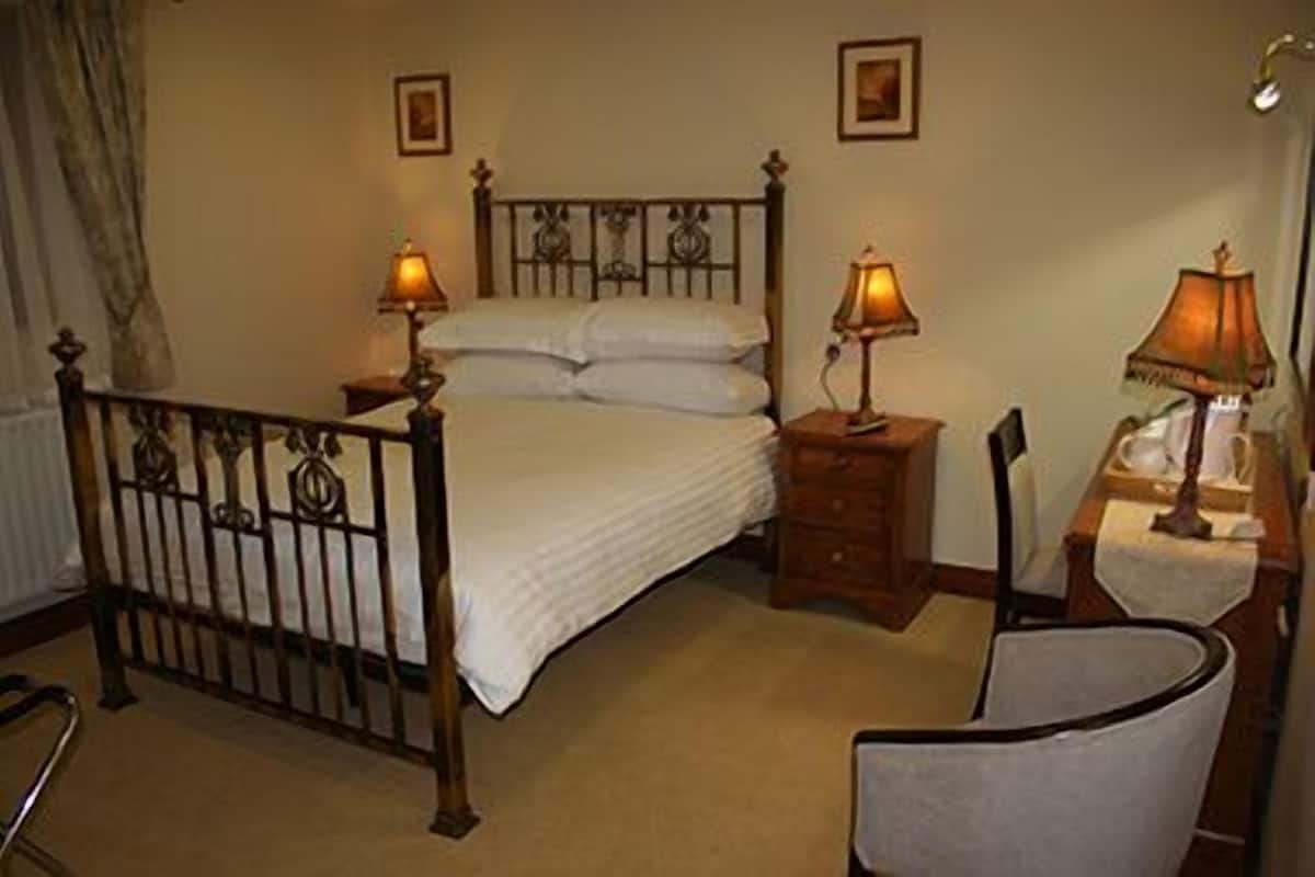 Quarto com cama, duas mesas de cabeceira com abajures, uma cadeira e um radiador.
