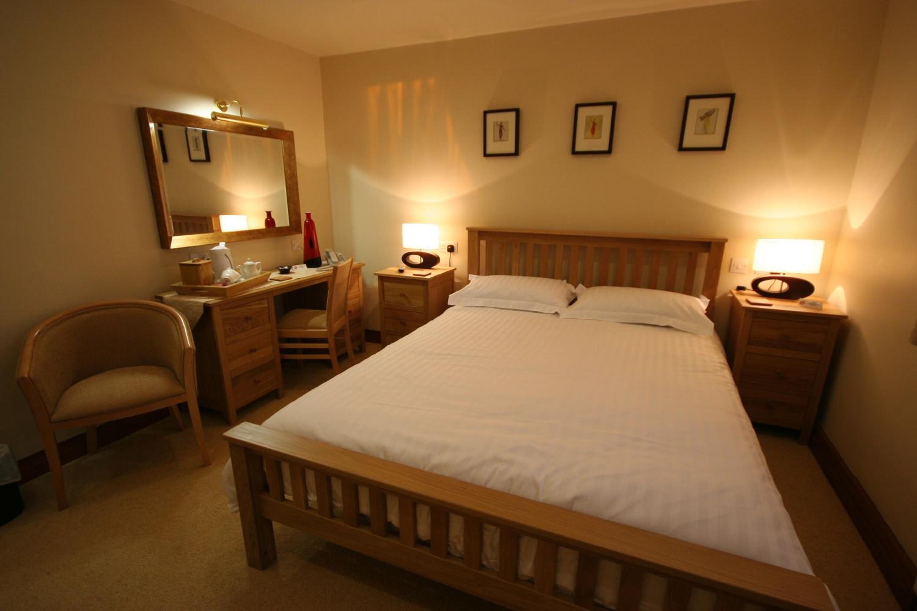 A hotel room with a wooden bed, a desk with a chair, a mirror, and bedside lamps.