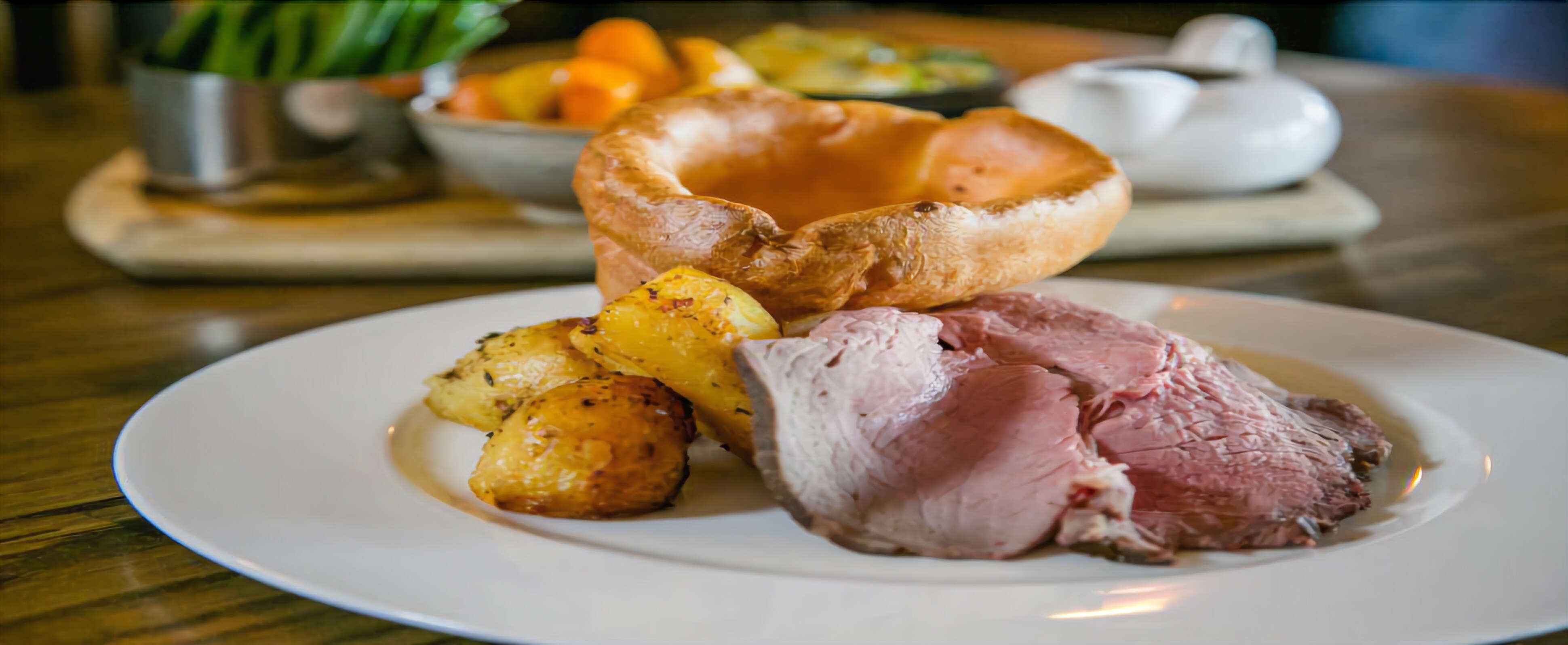 A plate with roast beef, roasted potatoes, and Yorkshire pudding.