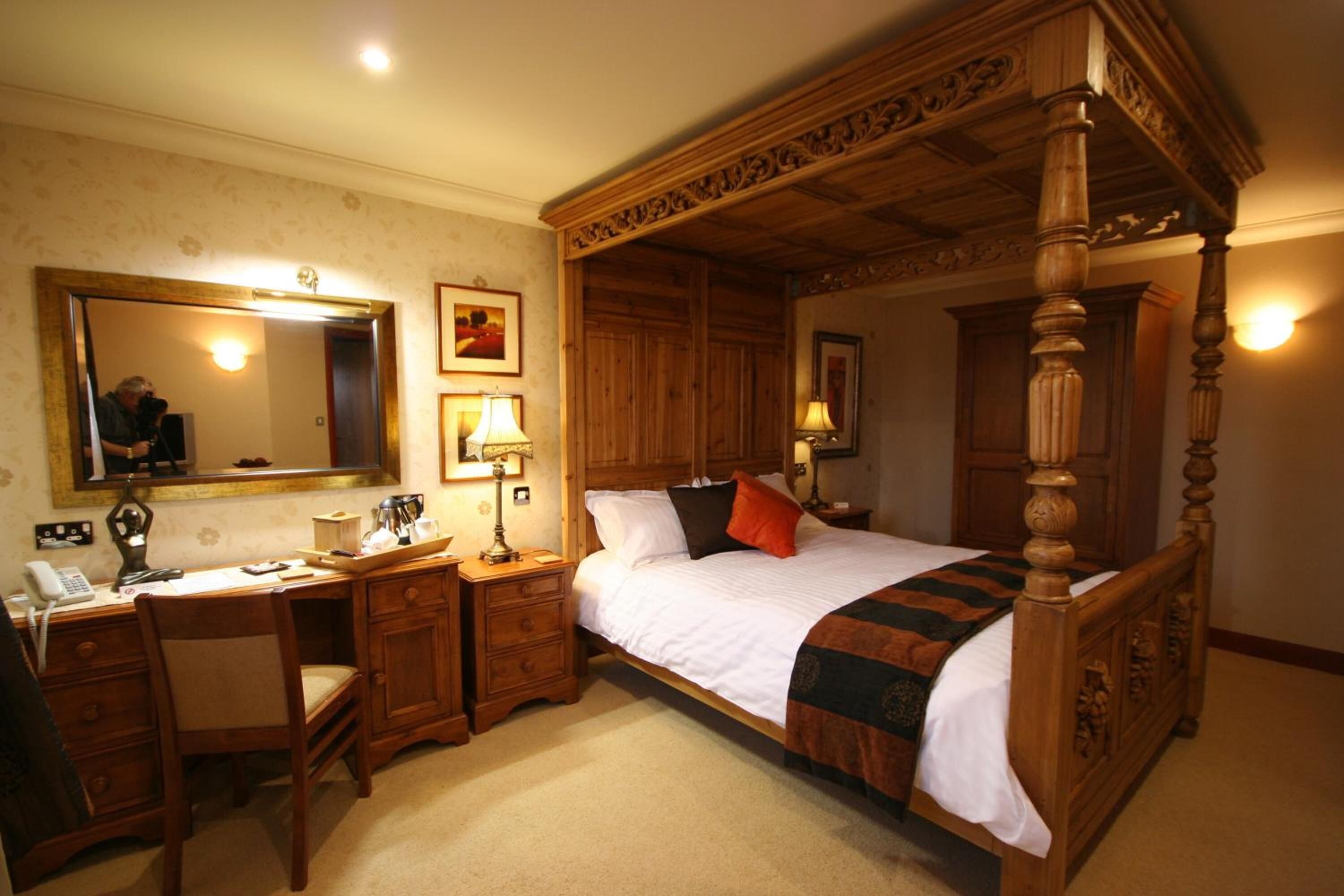 Una cama con dosel y tablero de madera, un escritorio con silla, un espejo y dos lámparas de noche.