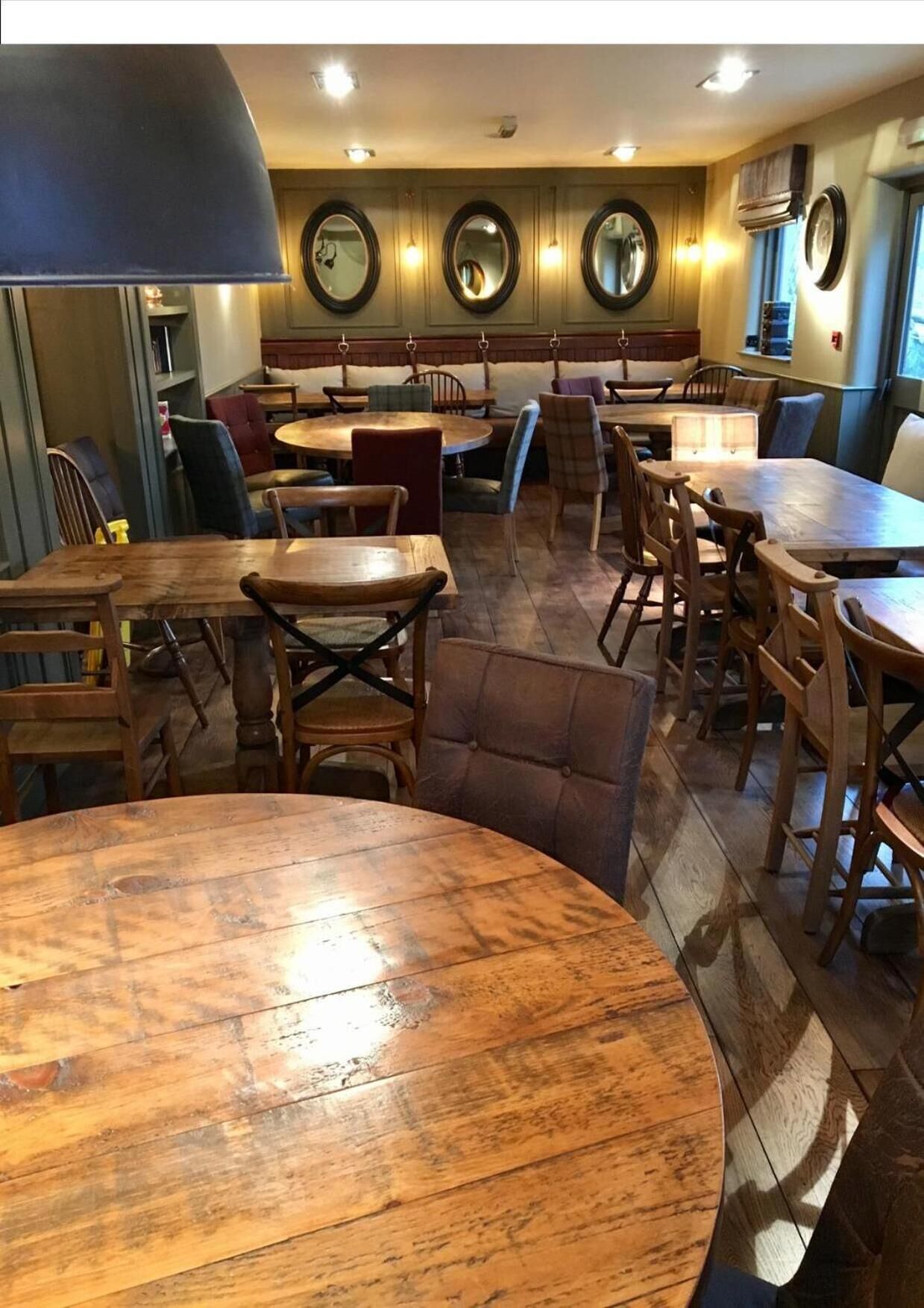 Un interior de restaurante con mesas y sillas de madera, una barra y una pared con espejos circulares.