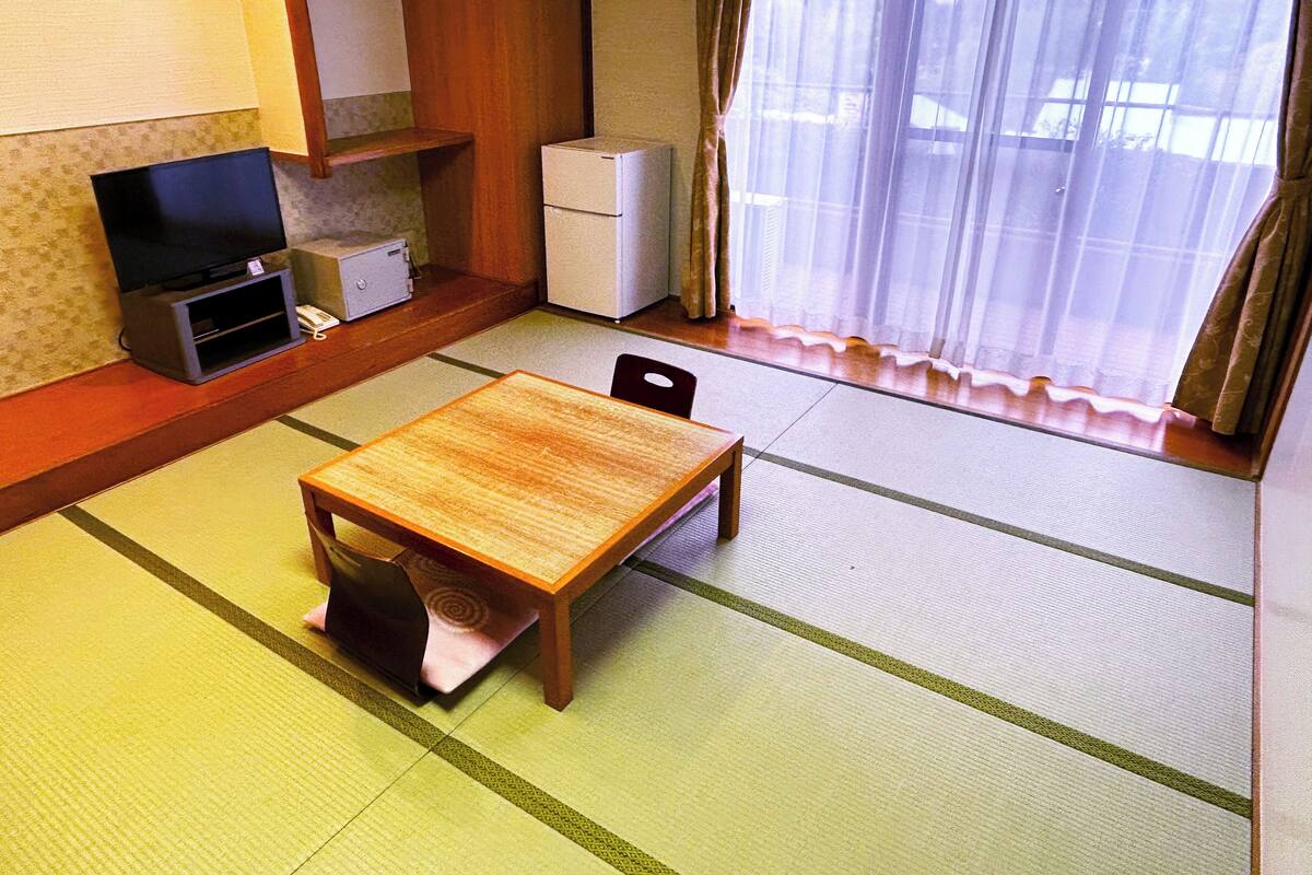 A room with tatami flooring, a wooden table, a television, and a refrigerator.