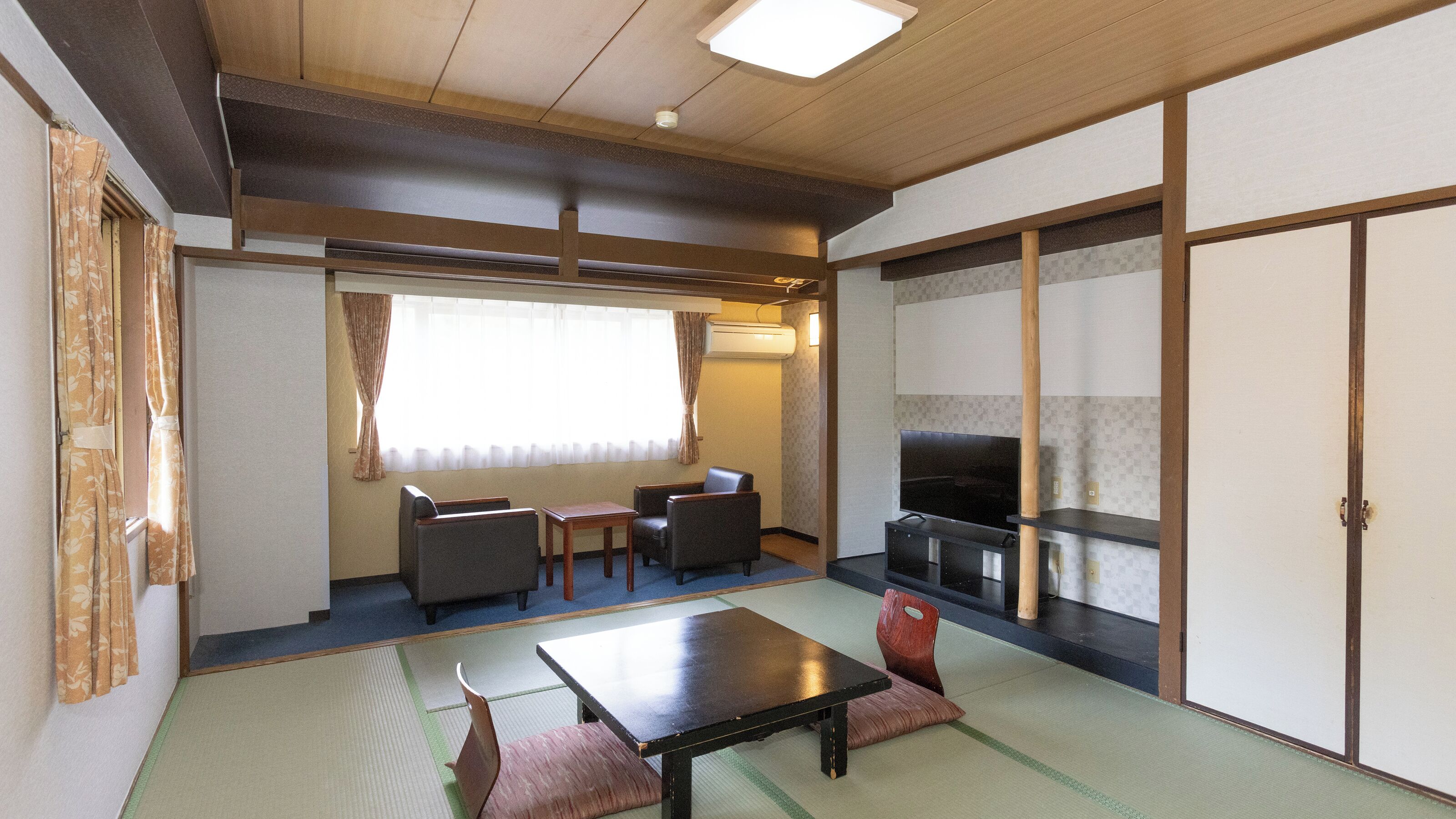 A traditional Japanese room with tatami flooring, a low table, two chairs, a television, and sliding doors.