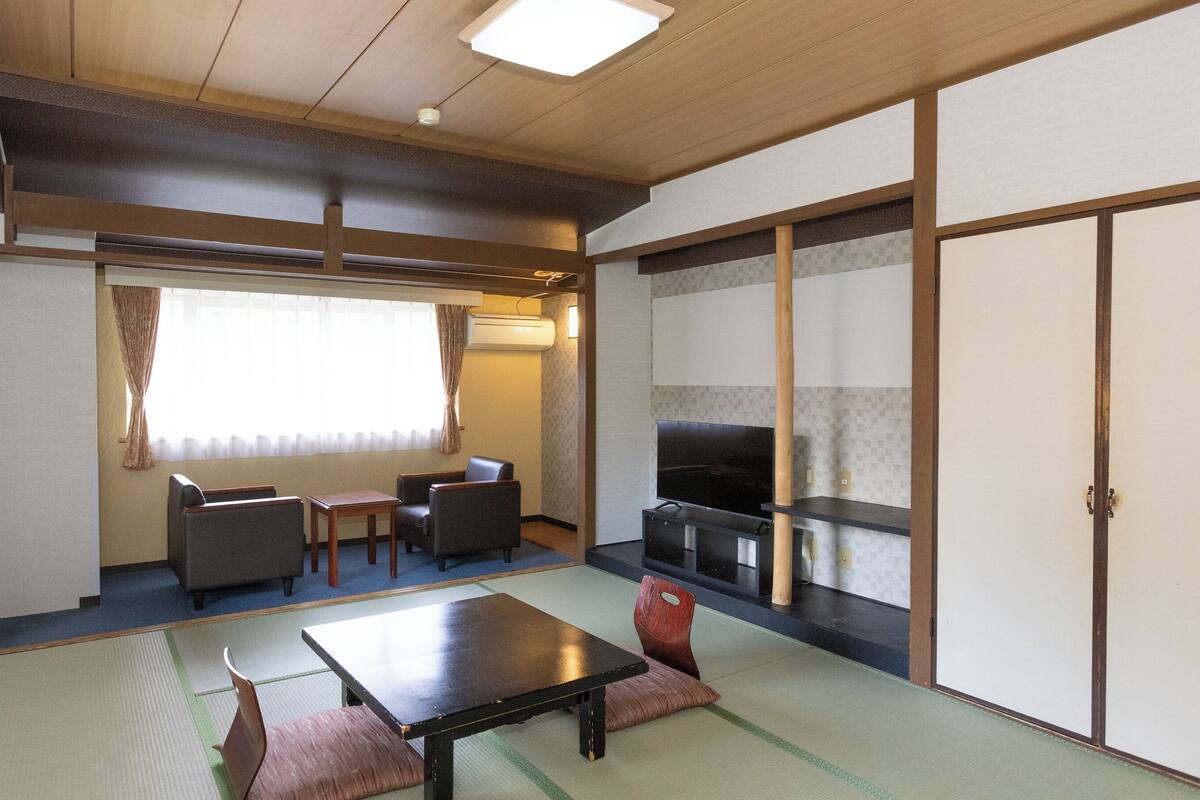 A traditional Japanese room with tatami flooring, a low table, two chairs, a television, and sliding doors.