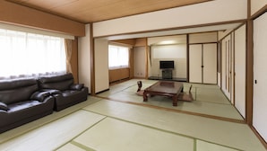 Une pièce de style japonais traditionnel, avec un sol recouvert de tatamis, un canapé, une télévision et des portes coulissantes.