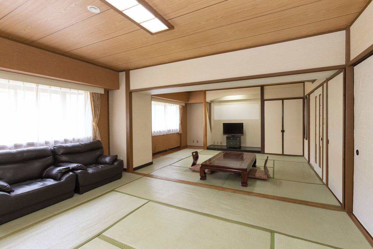 A traditional Japanese room with tatami flooring, a sofa, a TV, and sliding doors.