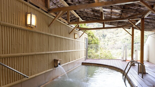Un onsen japonais traditionnel, avec des poutres en bois, des murs en bambou et une terrasse en bois.