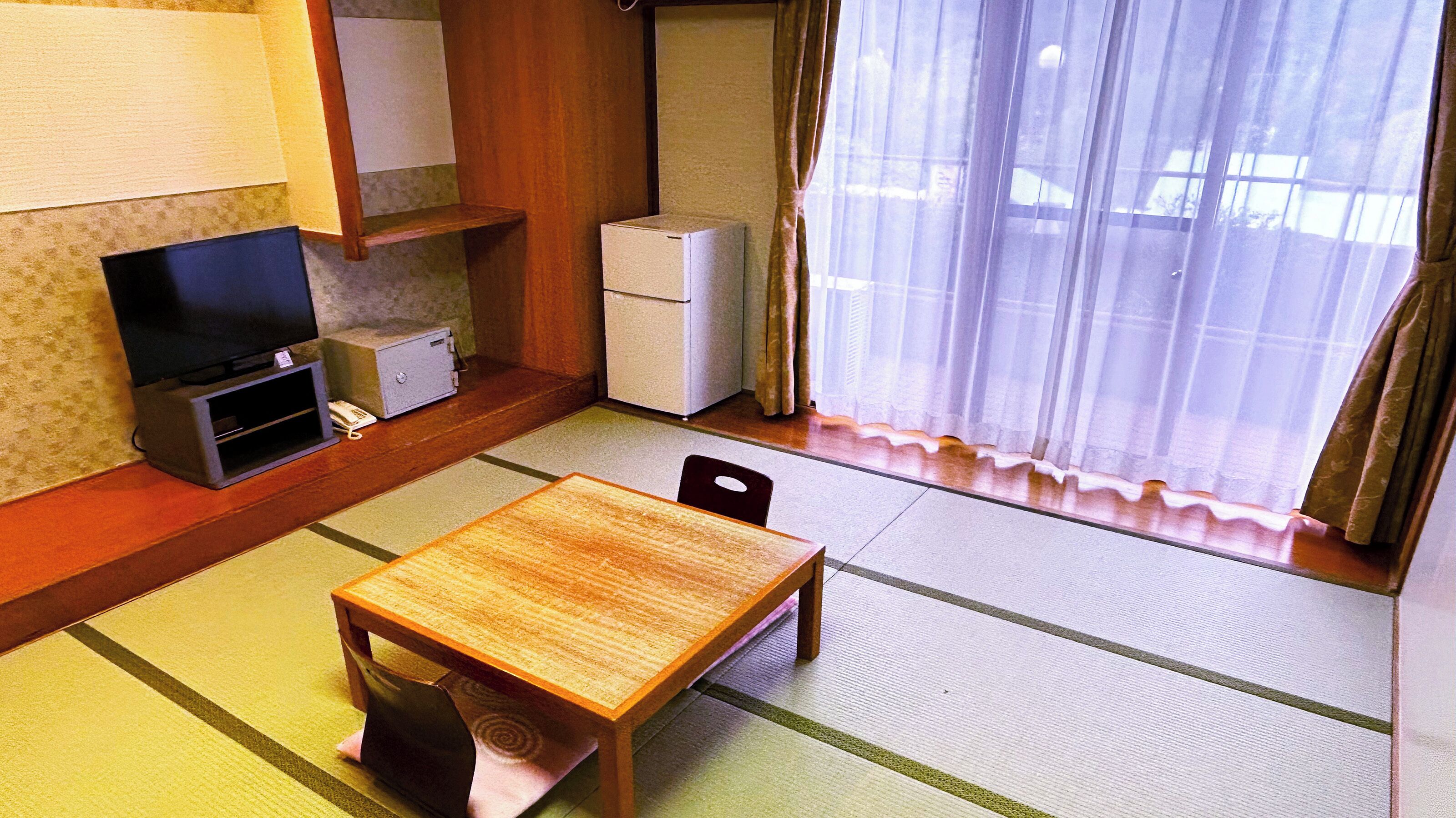 A small room with a wooden table, chairs, a television, a refrigerator, and a window with curtains.