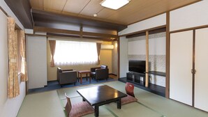 Une pièce de style japonais traditionnel, avec un sol recouvert de tatamis, une table basse, des sièges et un téléviseur.