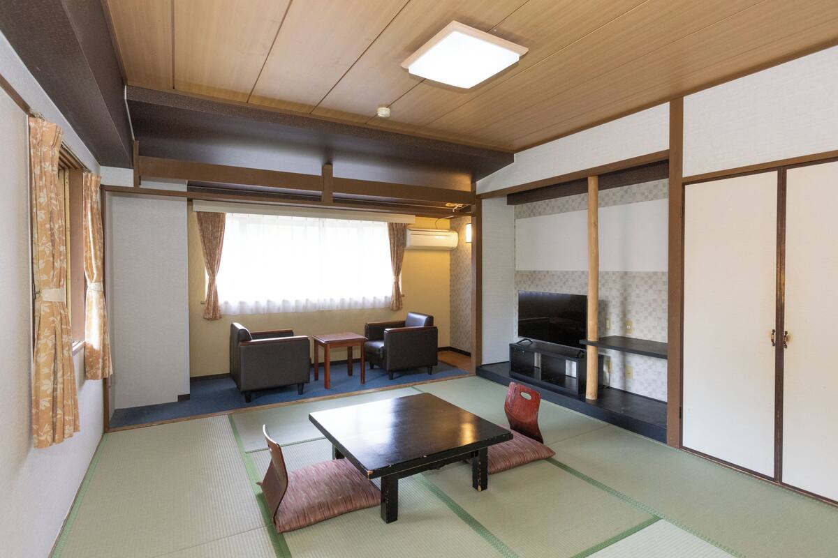 A traditional Japanese room with tatami flooring, a low table, seating, and a TV.