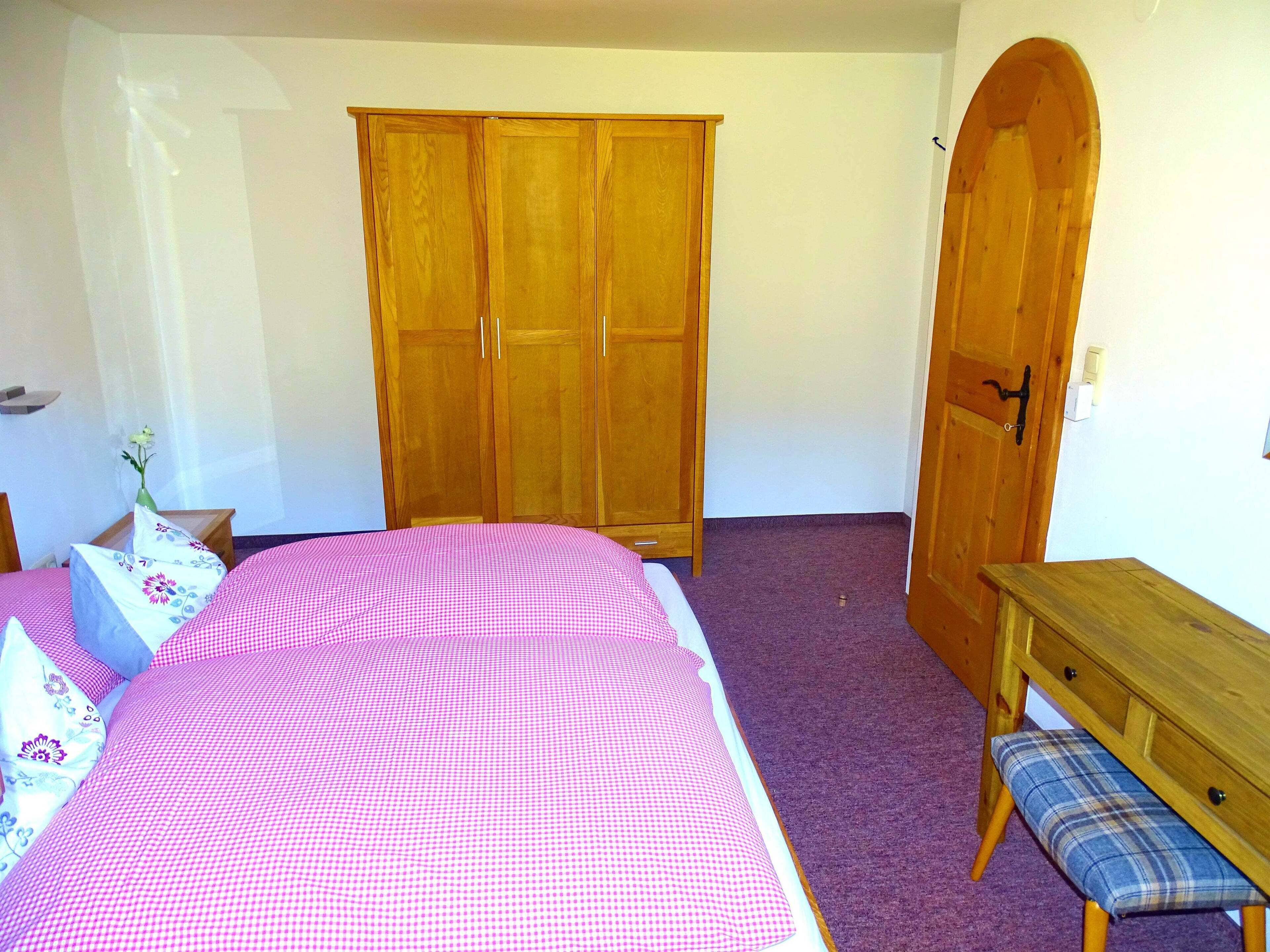 Une chambre à coucher avec un lit, une armoire en bois, un banc et une porte.