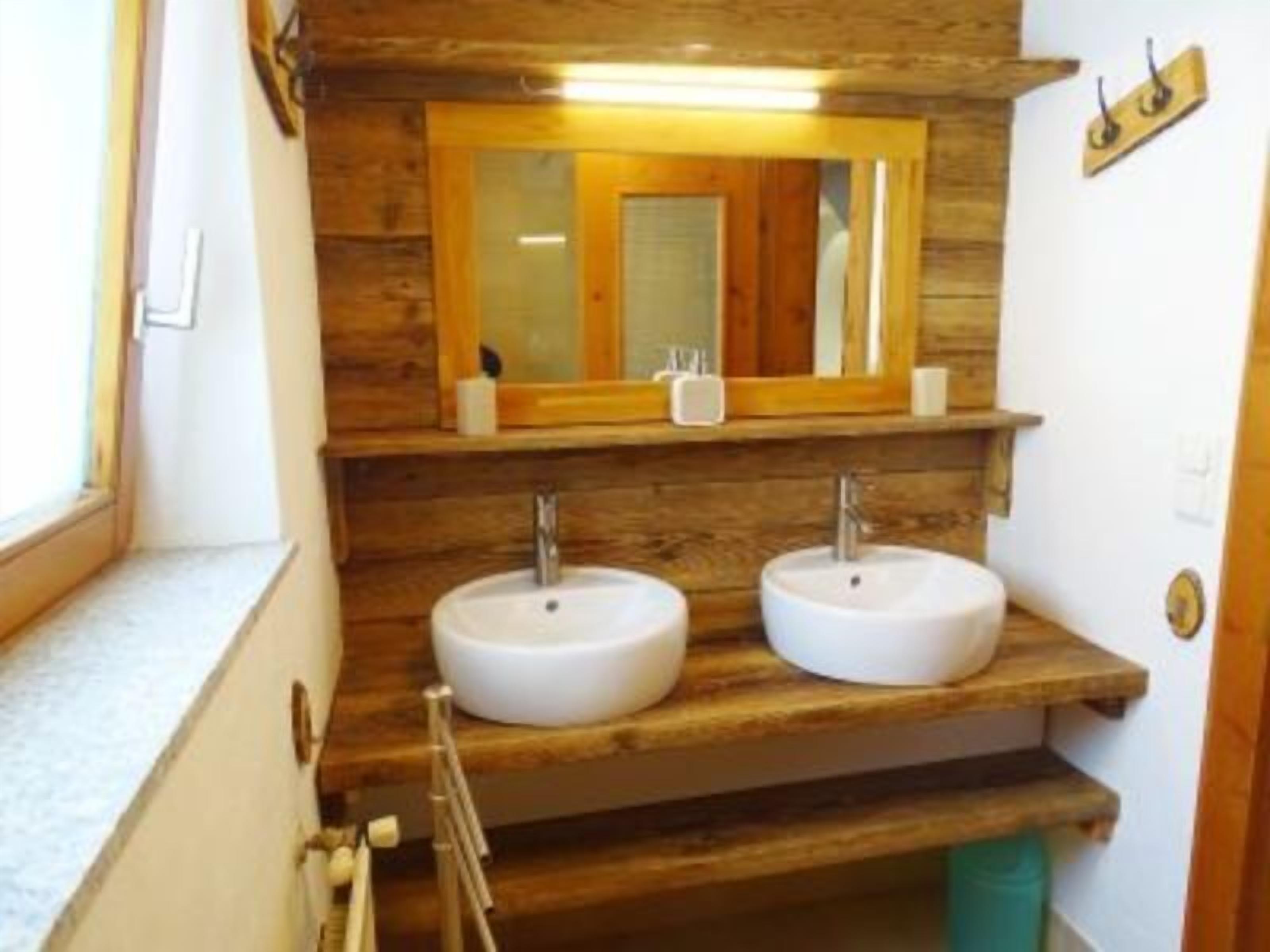 Un baño con detalles de madera, dos lavamanos, un espejo y una ventana.