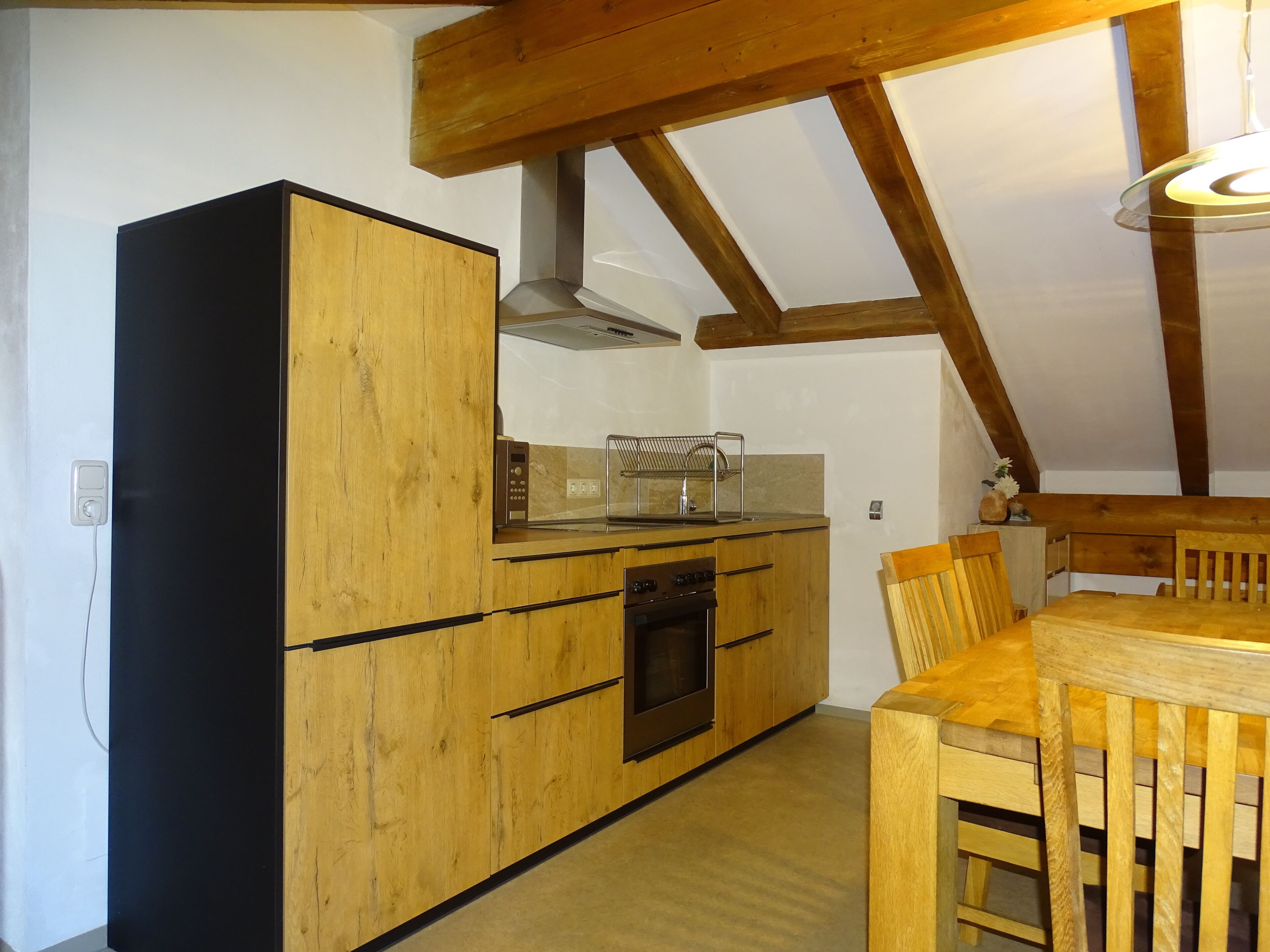 Una cocina con armarios de madera, horno empotrado y una mesa de comedor con sillas.