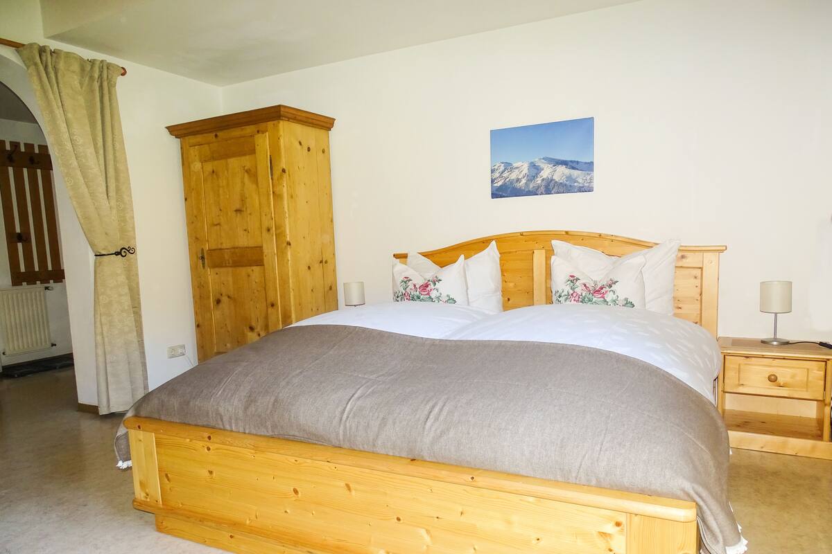 A bedroom with a wooden bed, a wooden wardrobe, a nightstand, and a wall-mounted picture of a mountain.