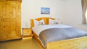 Un dormitorio con una cama de madera, una mesita de noche, un armario de madera y una pintura de montañas en la pared.