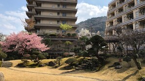 A multi-story building with balconies, surrounded by a landscaped garden with cherry blossoms and rocks. - Atami Kinjokan (Atami)
