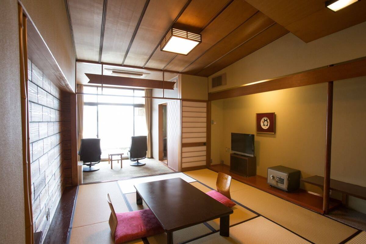 A traditional Japanese room with tatami flooring, a low table, chairs, a television, and a radio.