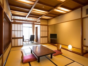 A traditional Japanese room with tatami flooring, a low table, a TV, and a sliding door leading to another room. - Atami Kinjokan (Atami)