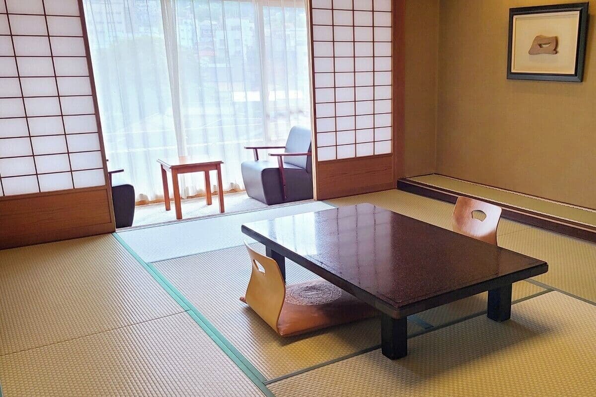 A tatami mat room with a low table and cushions, a sliding door, and a framed picture on the wall.