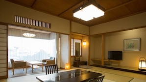 A traditional Japanese room with tatami flooring, a low table, chairs, a television, and a large window with a city view. - Atami Kinjokan (Atami)