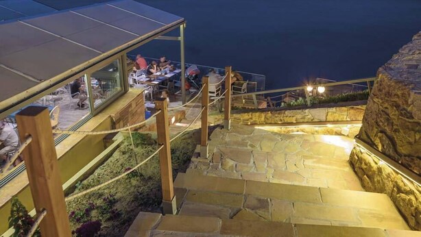 Un restaurante con terraza al aire libre, escalones de piedra y un cerramiento de cristal.