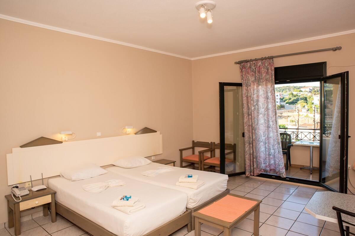 A hotel room with a bed, bedside tables, a chair, a small table, and a balcony with a view.