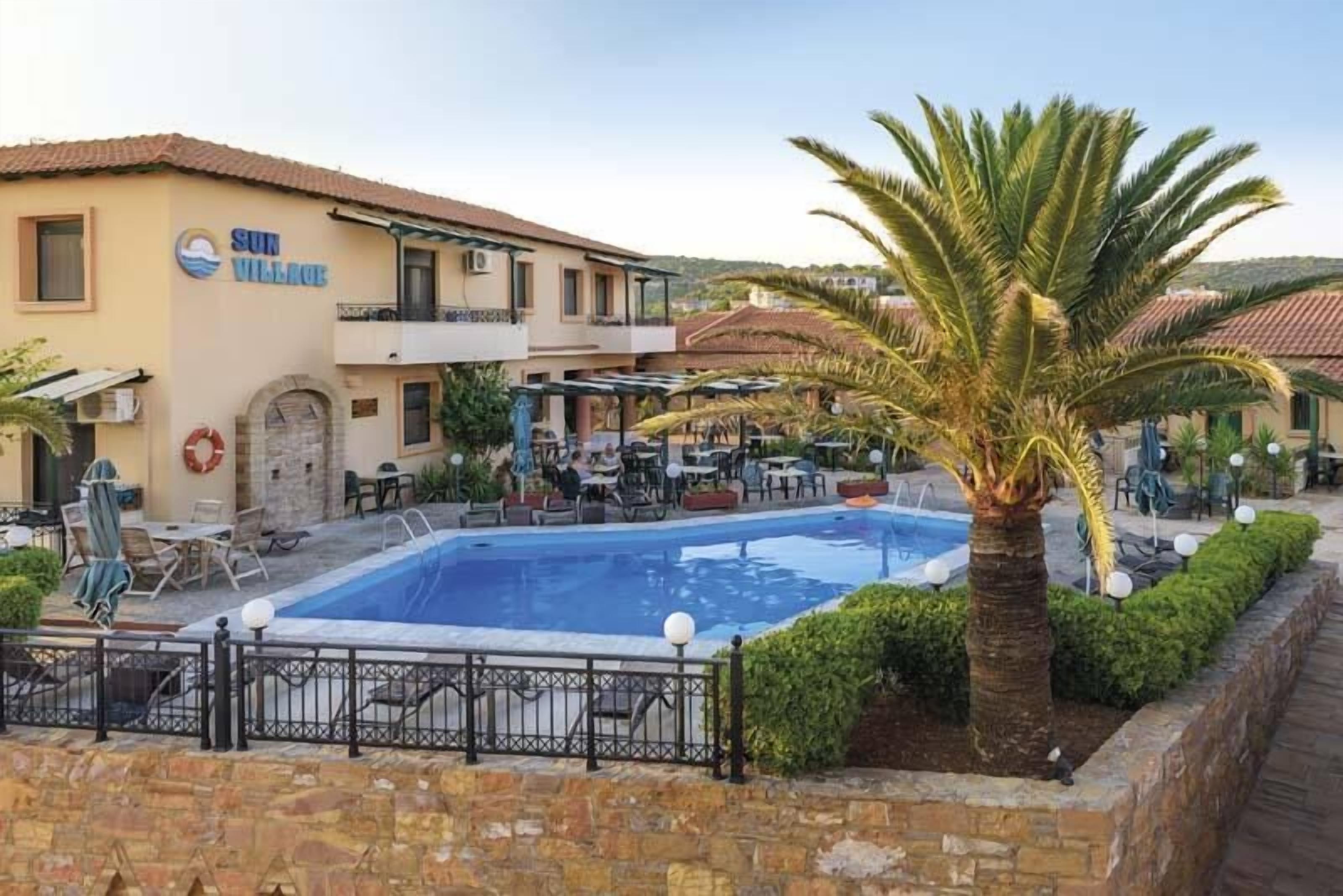 Um hotel com piscina, área de estar externa e uma palmeira.