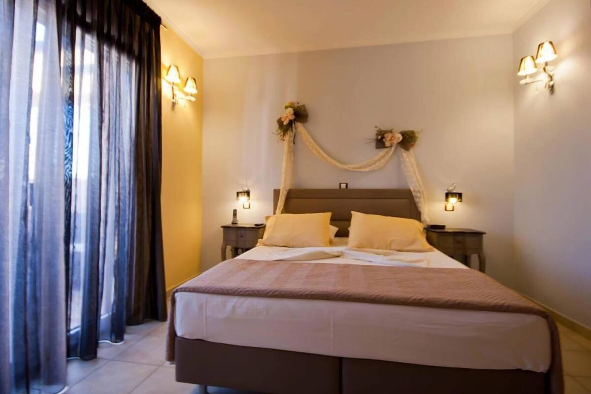 A hotel room with a bed, two bedside tables, a nightstand, a curtain, and wall-mounted lights.