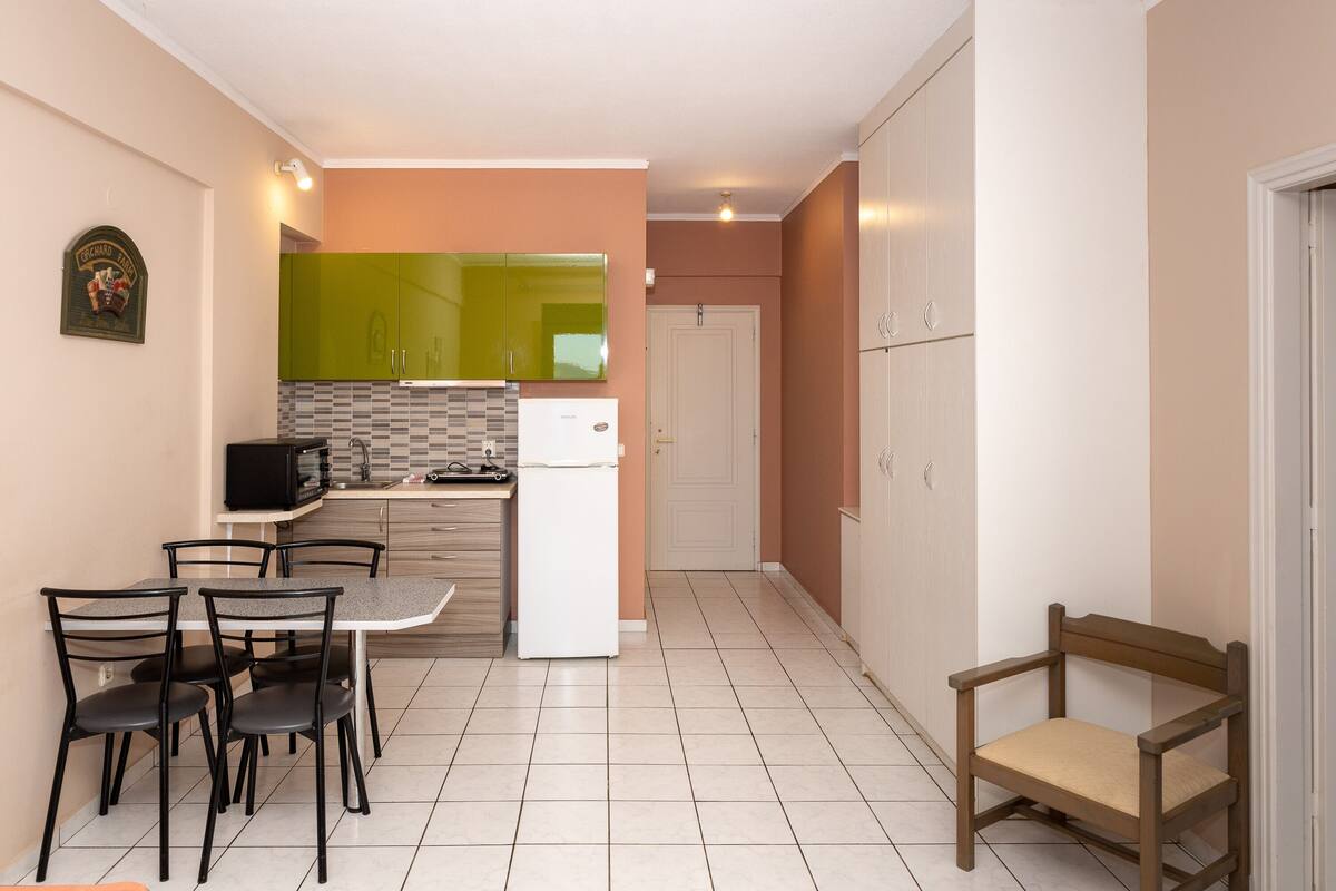 A compact kitchen with a dining table, chairs, a refrigerator, and cabinets.