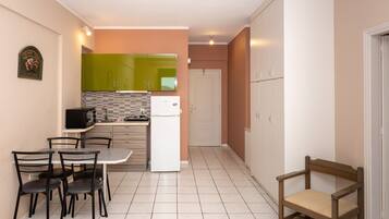A compact kitchen with a dining table, chairs, a refrigerator, and cabinets.