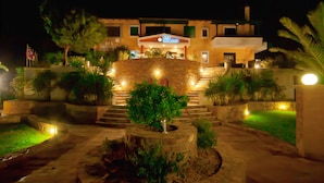 Un hotel con fachada de piedra, un letrero que dice "SUN VILLAGE" y una entrada bien iluminada con escalones que conducen al edificio principal.
