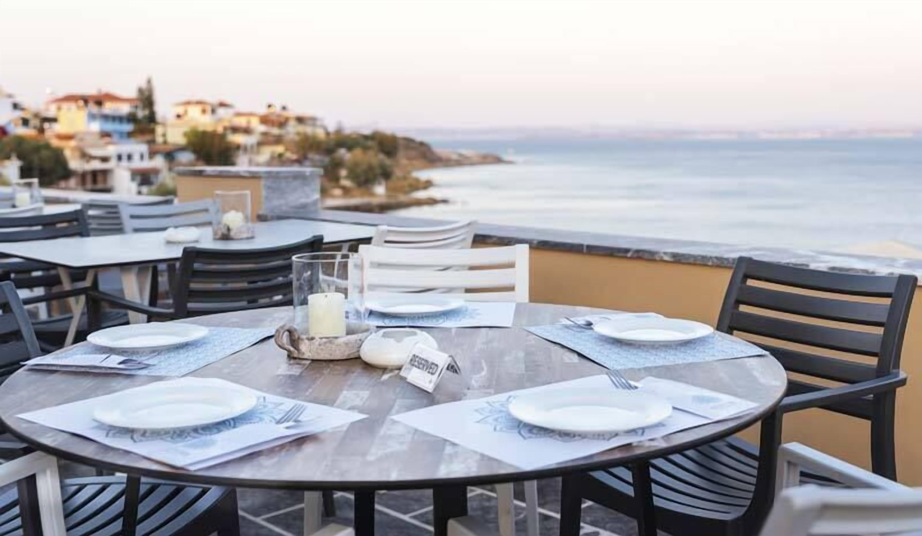 A round table set for four with plates, cutlery, and a candle, overlooking a coastal view.