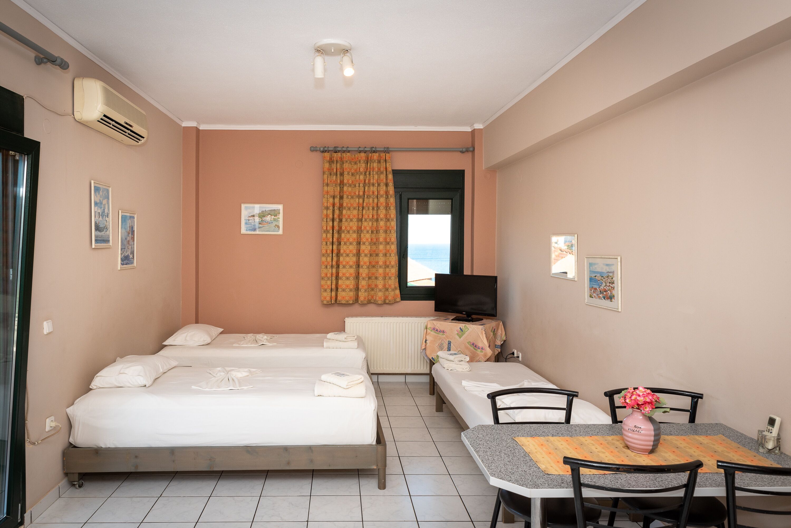 Habitación de hotel con dos camas individuales, una pequeña mesa con sillas, televisor y ventana con cortinas.