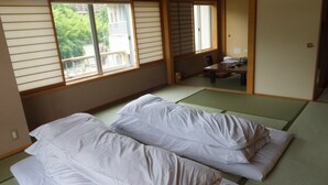 A traditional Japanese room with tatami flooring, a low table, and two beds with white bedding. - Itoen Hotel Shikisai (Yugawara)